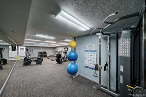 A gym with exercise equipment, a wall with a 'Please do not drop weights' sign, and a bulletin board with exercise images.
