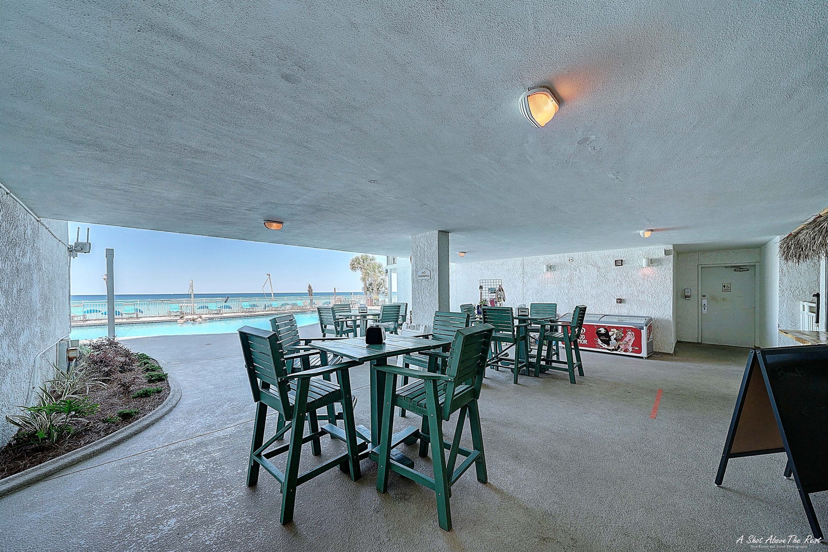 An outdoor seating area with tables and chairs, a pool in the background, and a view of the ocean.