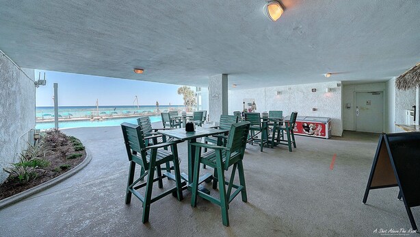 An outdoor seating area with tables and chairs, a pool in the background, and a view of the ocean.