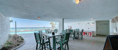 An outdoor seating area with tables and chairs, a pool in the background, and a view of the ocean.