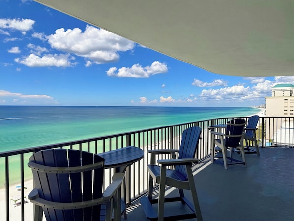 A balcony with a view of the ocean and a beach, featuring two chairs and a table.
