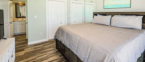 Un dormitorio con una cama grande, suelo de madera, ventilador de techo y un cuadro en la pared.