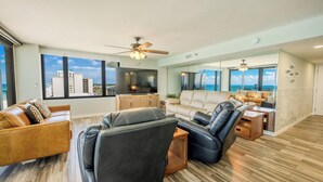 A spacious living area with a large flat-screen TV, leather sofas, and a view of the ocean through large windows.