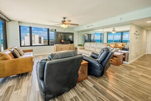 A spacious living area with a large flat-screen TV, leather sofas, and a view of the ocean through large windows.