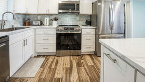 A modern kitchen with white cabinetry, stainless steel appliances, and a herringbone wood floor.