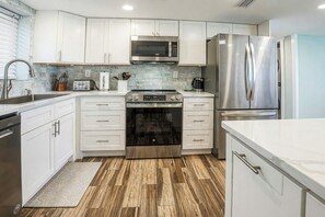 A modern kitchen with white cabinetry, stainless steel appliances, and a herringbone wood floor.
