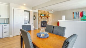 A dining area with a wooden table, grey upholstered chairs, and a stone fireplace.