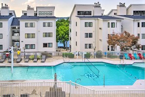 A swimming pool surrounded by white apartment buildings with balconies, a fenced deck area with lounge chairs, and a clear sky. - Relax Poolside! Lake-View Retreat in Osage Beach (Osage Beach)