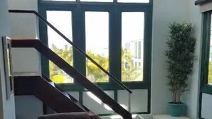 A living room with a brown sofa, a small table with a cup and a remote control, a potted plant, and a staircase leading to another room. - 5 pools, Amazing Rooftop Views , Beach (Vieques)
