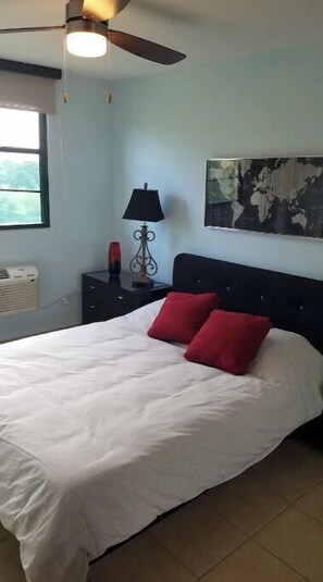 A bedroom with a bed, a nightstand, a lamp, a ceiling fan, a window, and a world map on the wall. - 5 pools, Amazing Rooftop Views , Beach (Vieques)