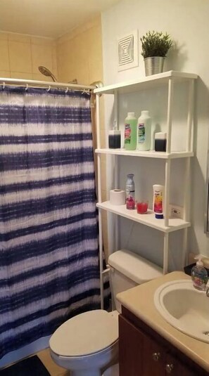 A bathroom with a striped shower curtain, a toilet, a sink with a mirror, and shelves with toiletries. - 5 pools, Amazing Rooftop Views , Beach (Vieques)