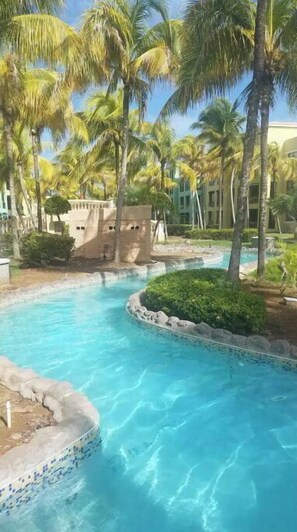 A swimming pool with clear blue water, surrounded by palm trees and a stone structure. - 5 pools, Amazing Rooftop Views , Beach (Vieques)