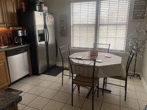 A kitchen with a dining table, chairs, a refrigerator, and a window with blinds. - The NashvilleNest 3BR 2Ba Large Fenced Yard 15 Min to DT (Nashville)