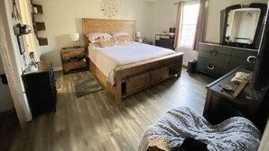 Une chambre à coucher avec un lit en bois, une commode, une table de chevet, un miroir et une fenêtre avec des rideaux.