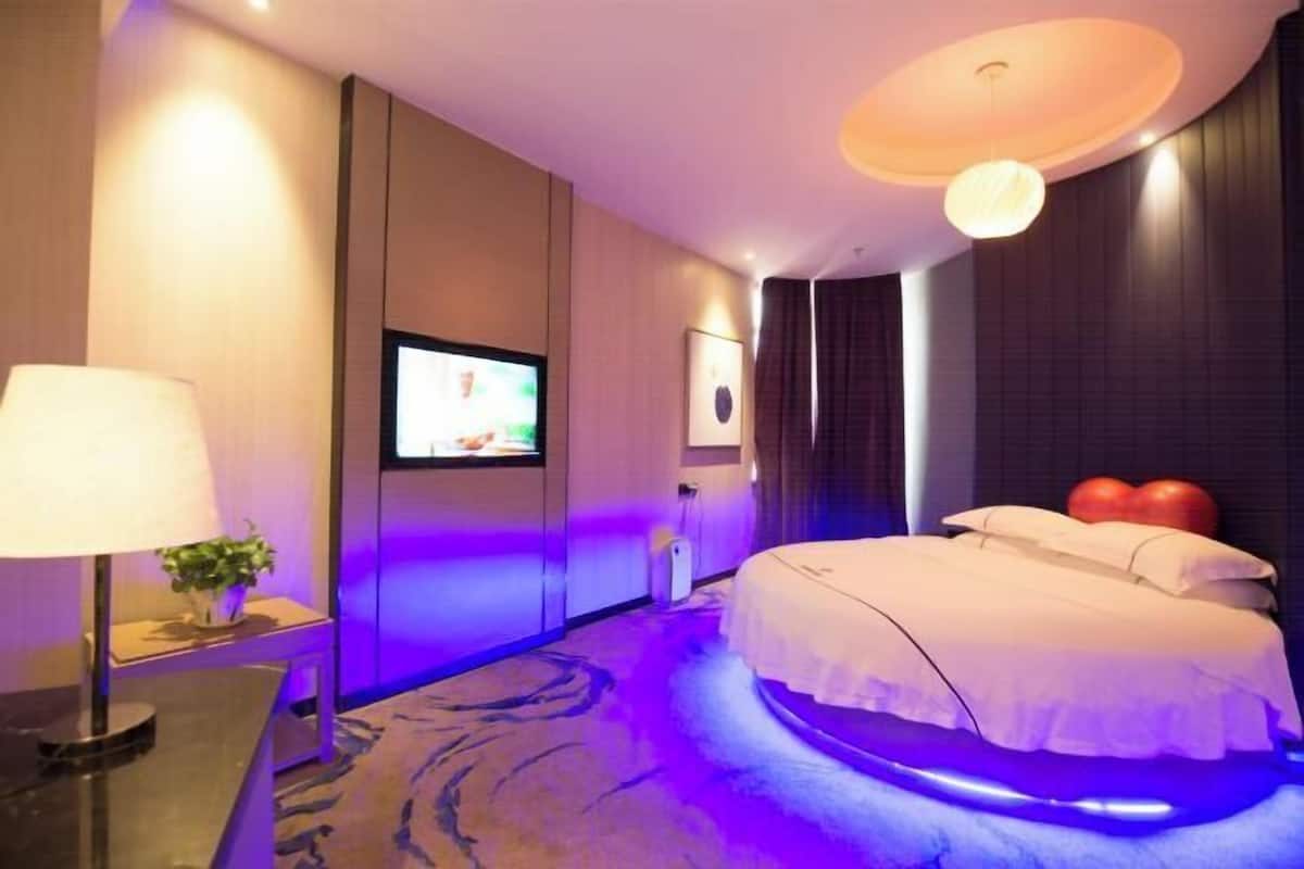 A hotel room with a bed, a TV, a lamp, and a plant.