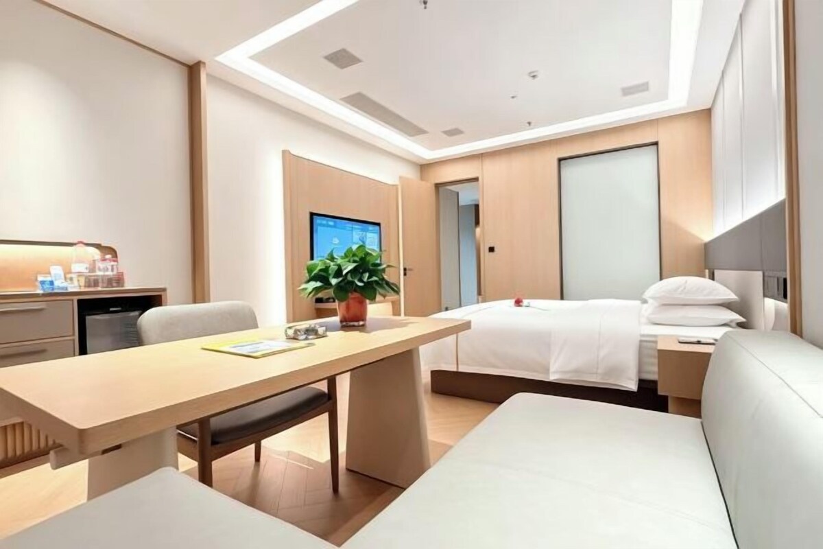 Habitación de hotel moderna con cama, escritorio, silla, sofá y planta en maceta.