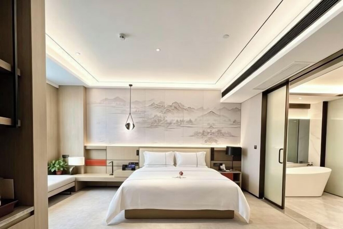 Una habitación de hotel moderna con una cama grande, mesitas de noche, un televisor montado en la pared y un baño con bañera.
