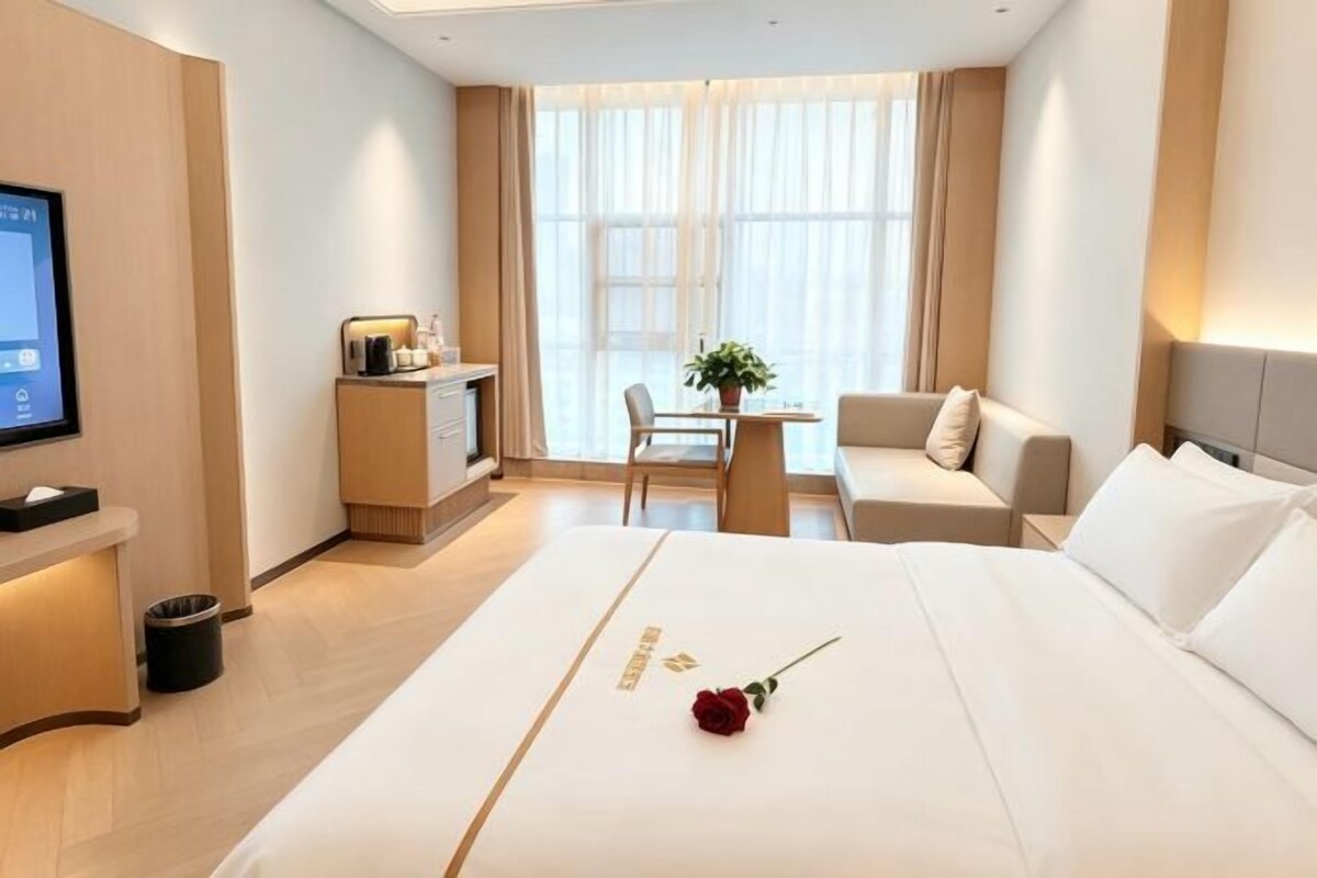 A hotel room with a bed, a desk, a chair, a TV, and a window with curtains.