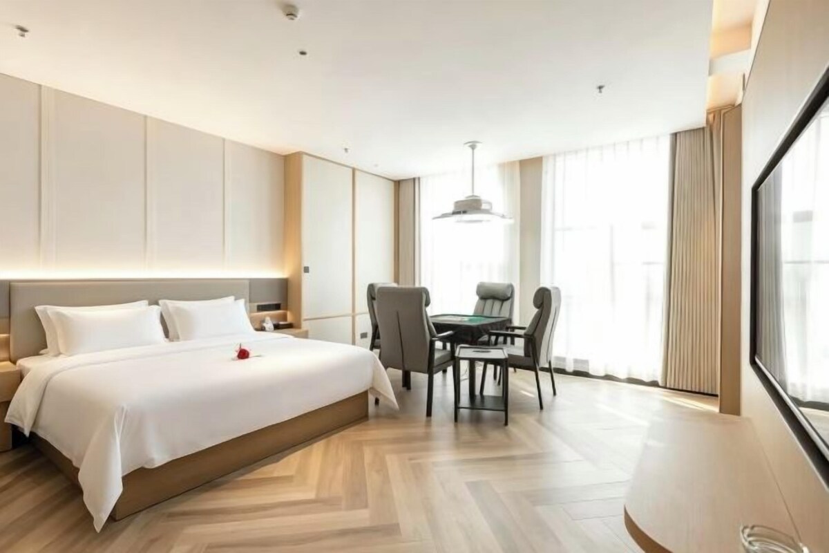 A hotel room with a large bed, a dining table with chairs, and a view of the outdoors.