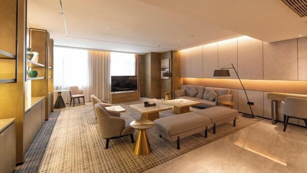 A modern hotel room with a living area featuring a sofa, coffee table, and armchairs. There is a TV, a lamp, and a bookshelf. - Huarong Hongfa International Hotel (People's Square) (Huarong)