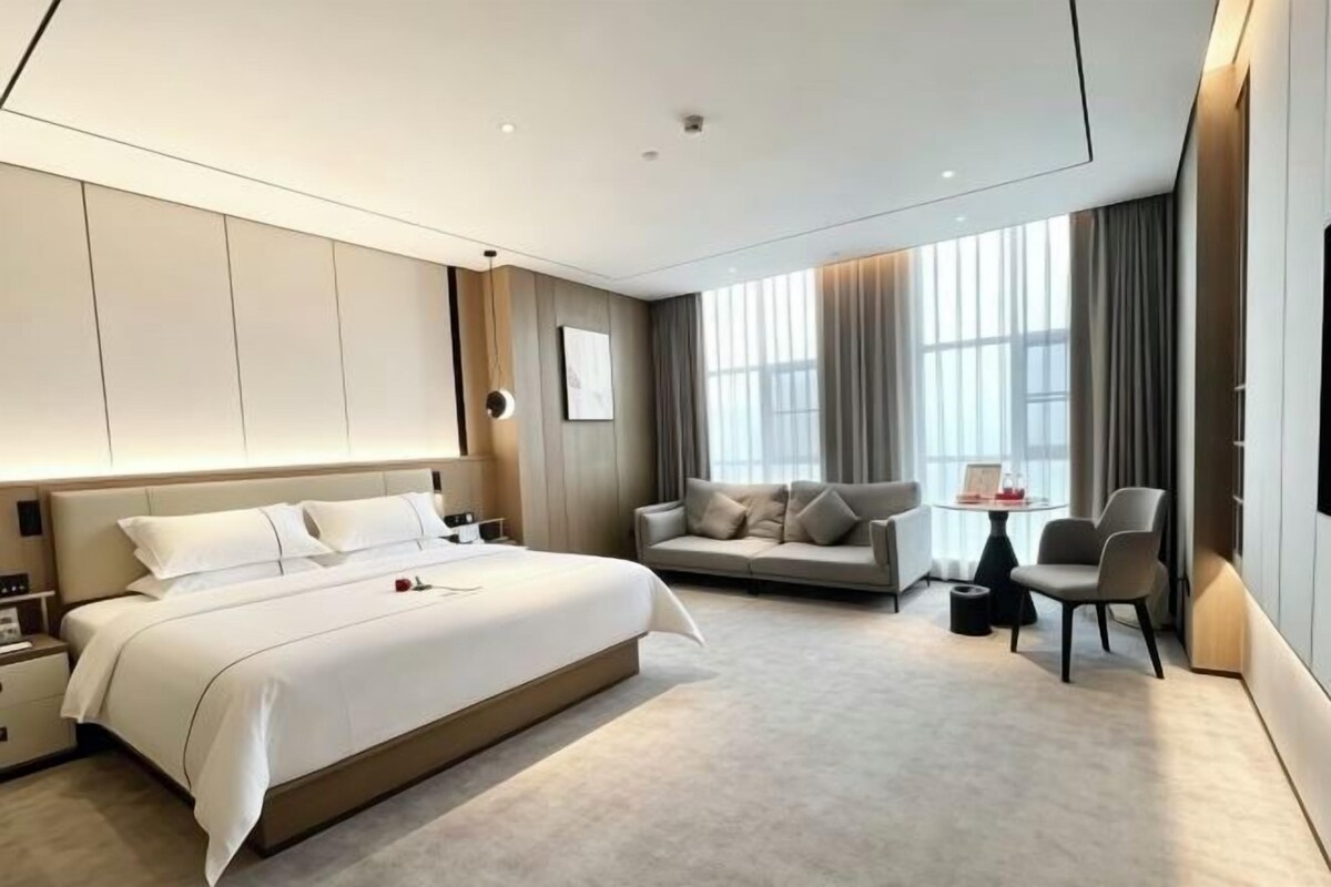 A modern hotel room with a large bed, a sofa, a small table, and a chair.