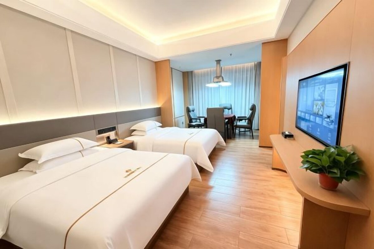 A hotel room with two beds, a desk, a chair, and a television.