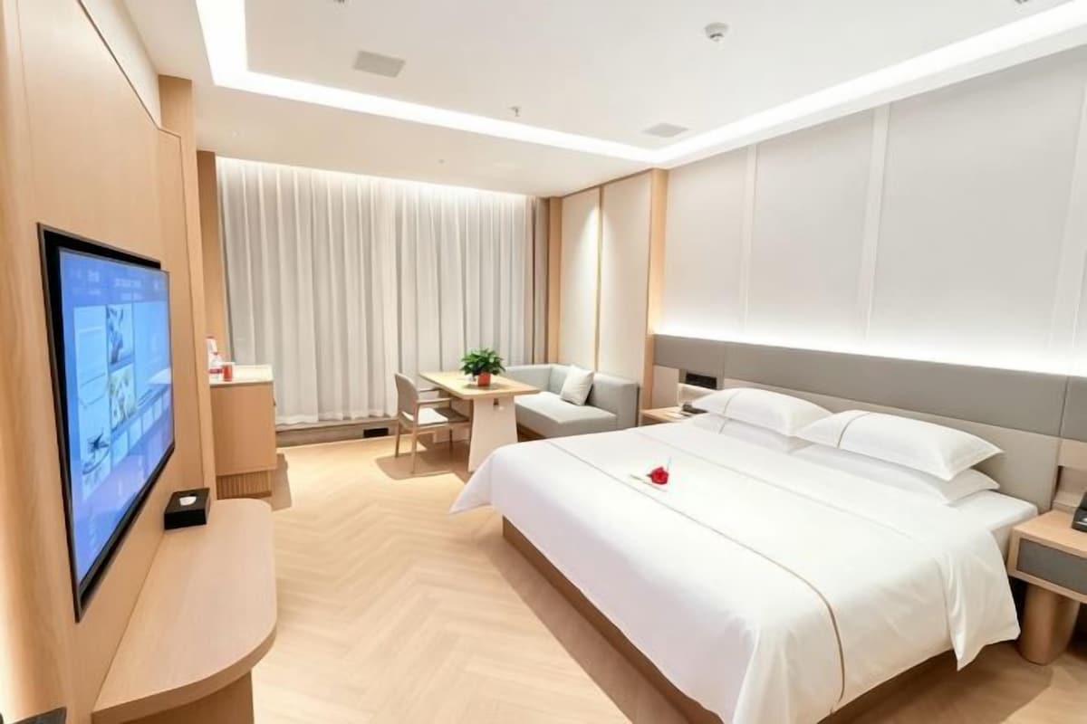 A modern hotel room with a large bed, a TV, a desk, and a seating area.