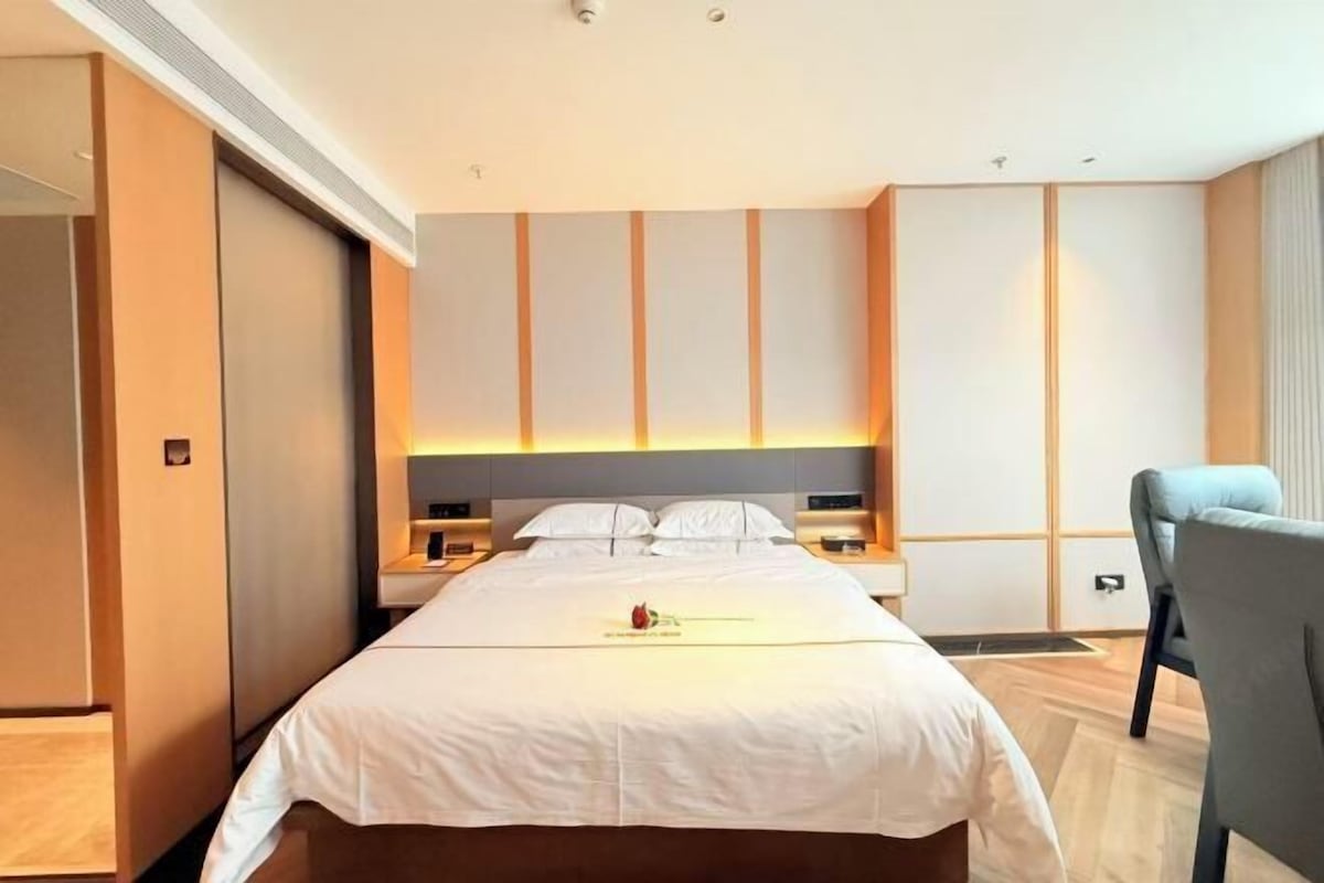A hotel room with a large bed, bedside tables, a chair, and a wardrobe.