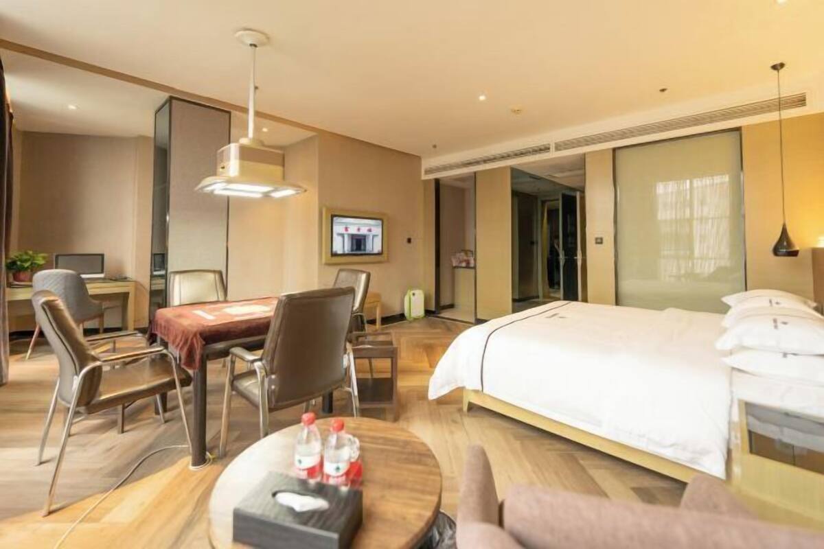 Una habitación de hotel con una cama, un escritorio con una silla, una mesa con dos botellas y un televisor en la pared.