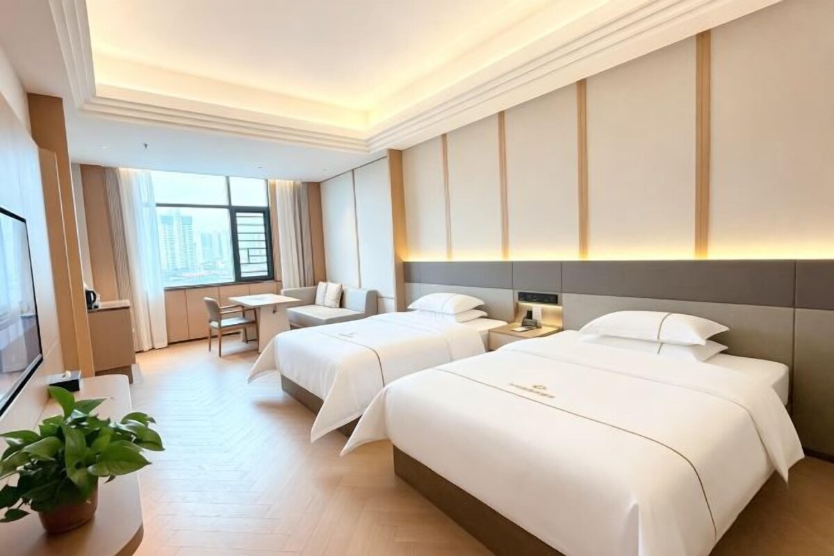 A hotel room with two beds, a desk, a chair, and a large window.