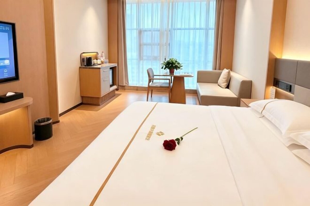 A hotel room with a bed, a desk, a chair, a TV, and a window with curtains.