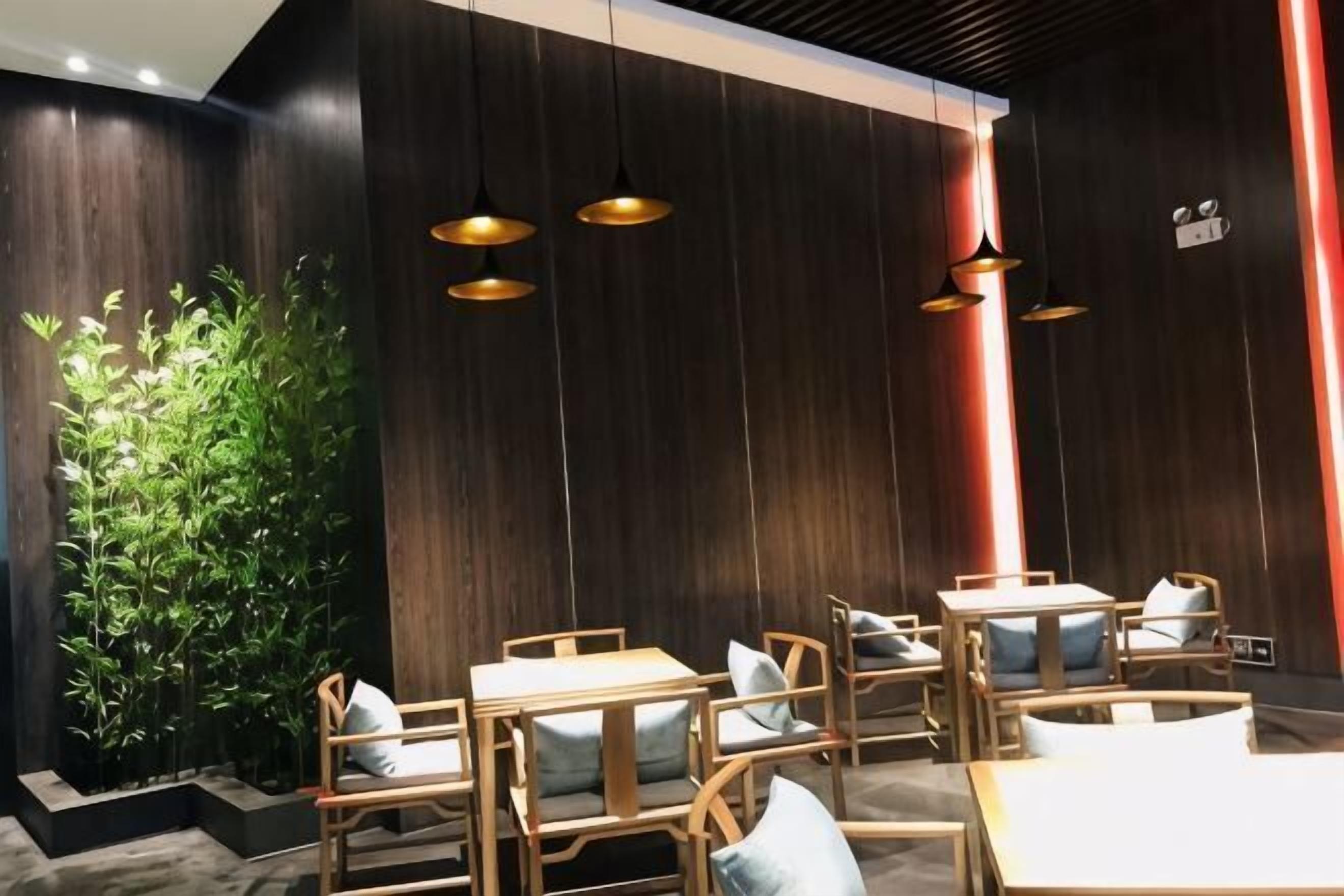 Ein Restaurantinnenraum mit Holztischen, Pendelleuchten und einer vertikalen Begrünung.