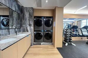 A modern gym with a marble wall, a mirror, a washing machine, and exercise equipment. - Huarong Hongfa International Hotel (People's Square) (Huarong)