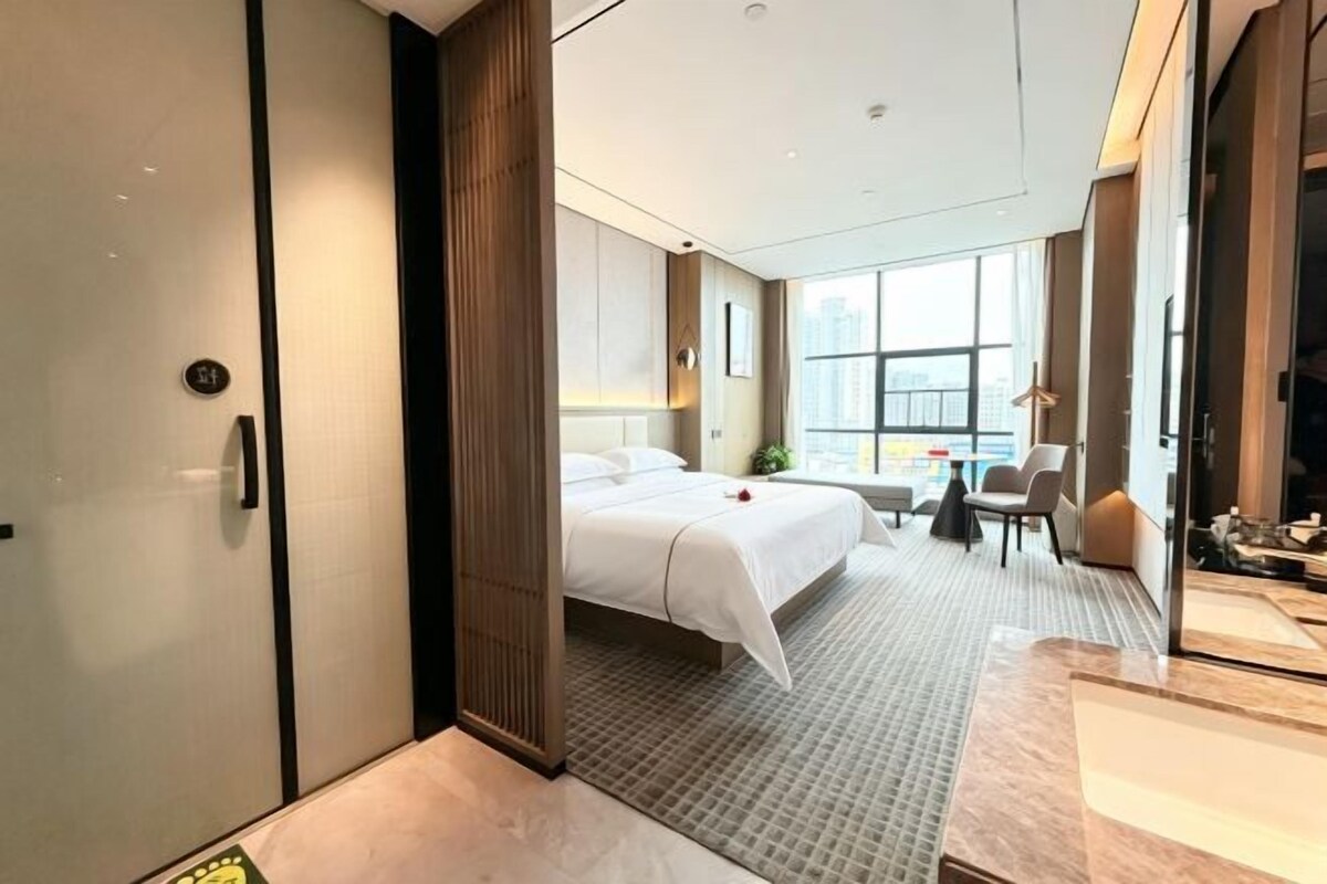 A modern hotel room with a bed, a desk, and a view of the city.