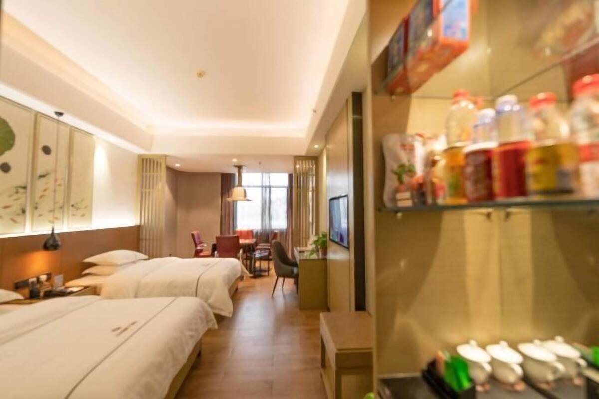 Habitación de hotel con dos camas, un escritorio y una zona de comedor. Hay botellas y vasos en un estante.