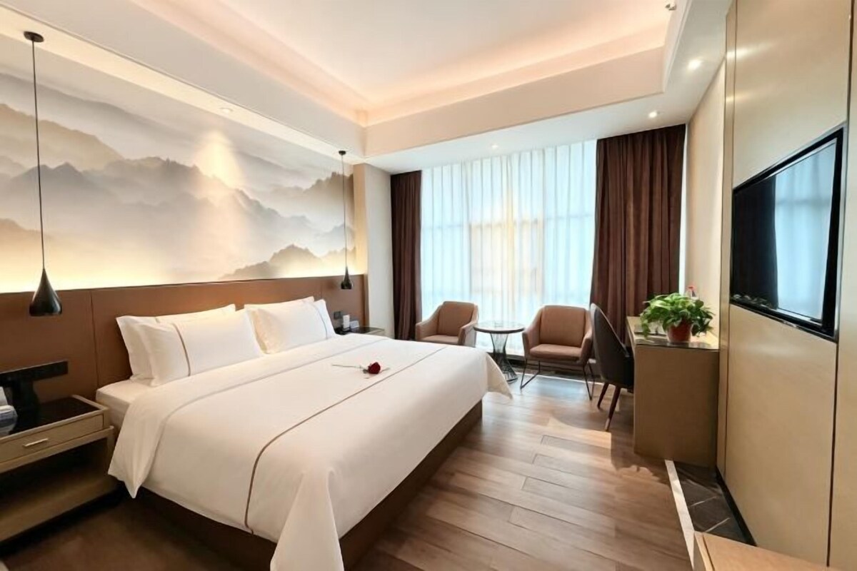 A hotel room with a large bed, a TV, a desk, and a seating area with a plant.