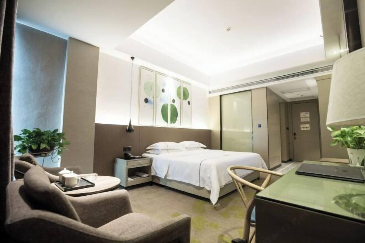 Una habitación de hotel moderna con una cama, un escritorio, una silla y una pequeña mesa con una taza y un platillo.