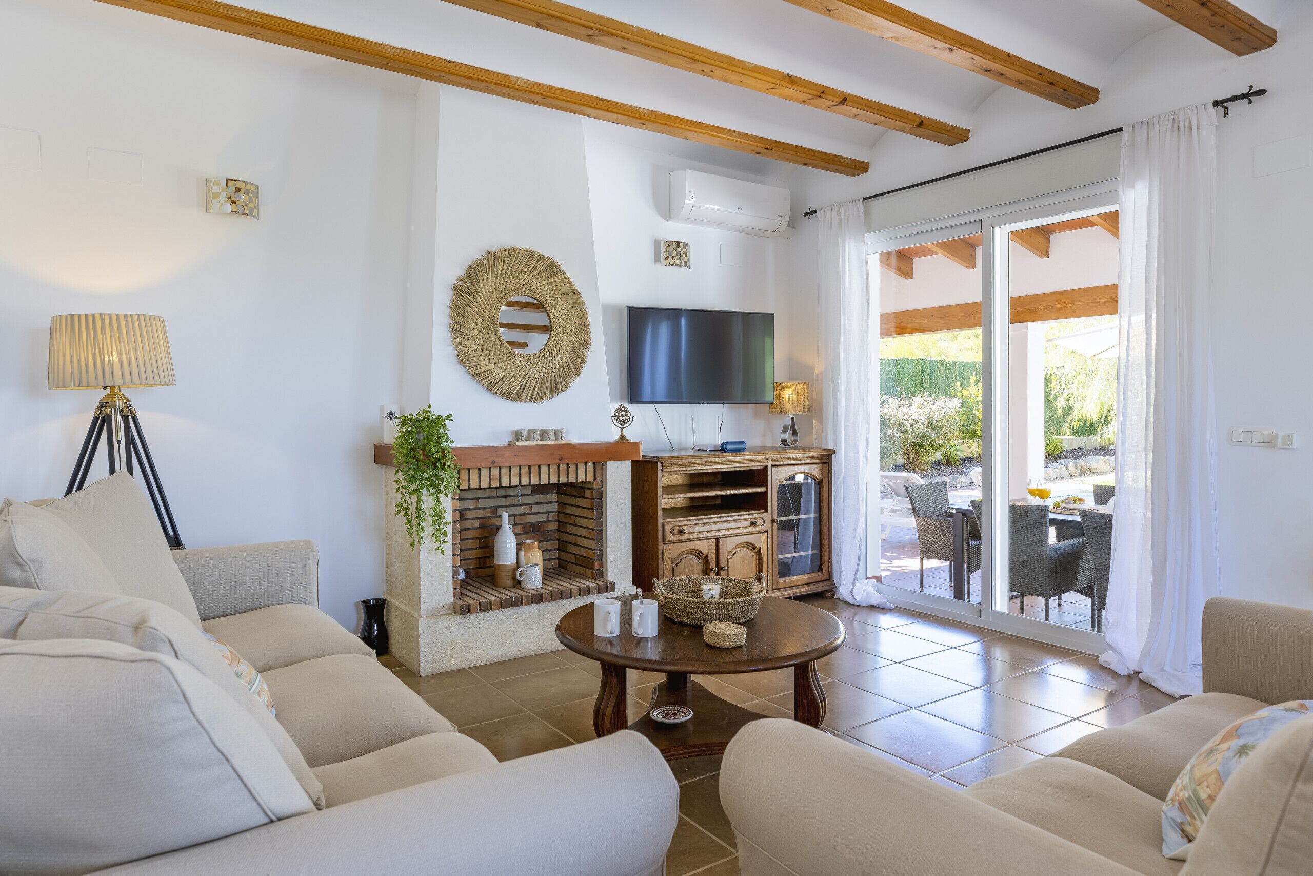 Una sala de estar con sofás, televisor, chimenea y comedor con mobiliario de exterior.