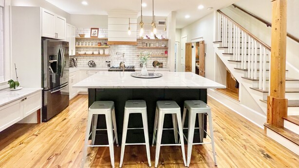 A modern kitchen with a large island, bar stools, stainless steel appliances, and wooden flooring.