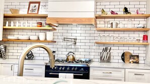A modern kitchen with white subway tiles, wooden shelves, and a gas stove.