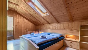 A bedroom with a skylight, wooden walls, a bed with pillows, a nightstand, and a wooden wardrobe.