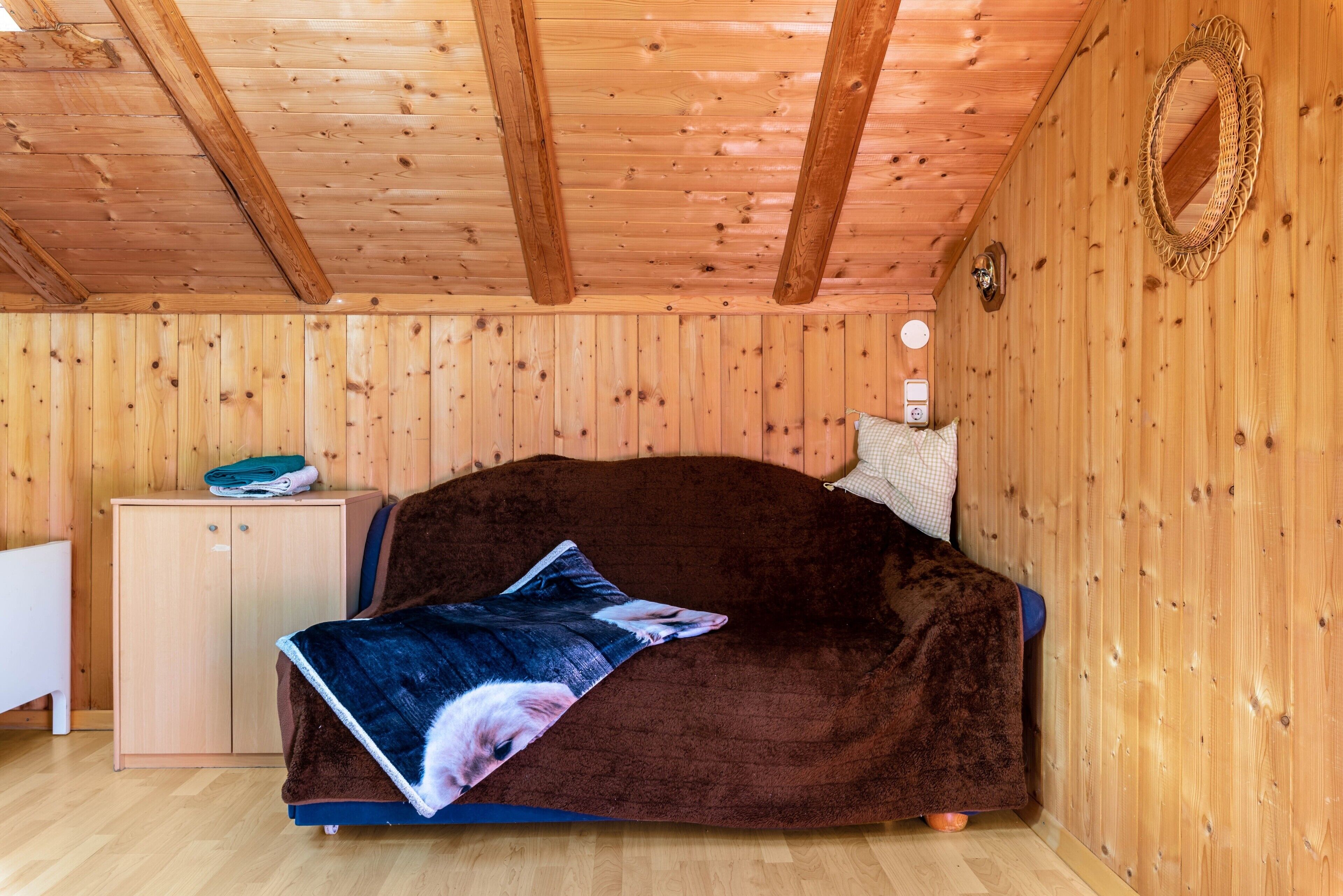 A cozy room with a wooden ceiling, a bed with a blanket, a small cabinet, and a wall-mounted mirror.