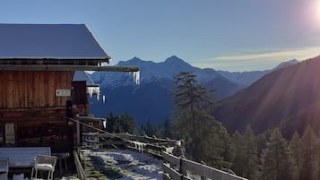 Eine Holzhütte mit schneebedecktem Dach, einer Holzterrasse und Blick auf die Berge.