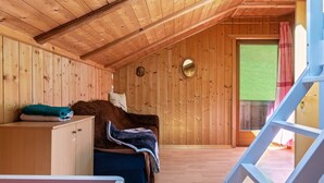 A wooden interior with a bed, a cabinet, and a window with a view of greenery.