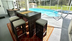 A covered outdoor area with a pool, wicker furniture, and a ceiling fan.