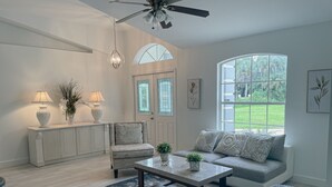 A spacious living room with a sofa, a coffee table, and a chair. There is a large window providing a view of the outdoors.