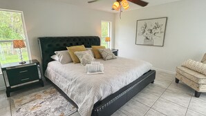 A bedroom with a large bed, a nightstand, a chair, a ceiling fan, and a window.