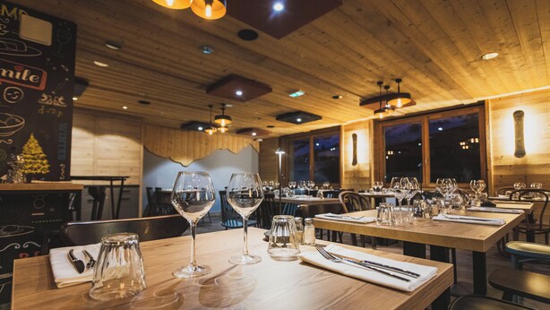 Ein Restaurant mit Holzvertäfelung, gedeckten Tischen inklusive Weingläsern und Besteck sowie einer gemütlichen Atmosphäre.