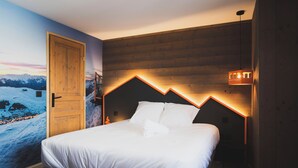 Un dormitorio con cabecera de madera, cama con ropa de cama blanca, mesita de noche y lámpara fijada a la pared.
