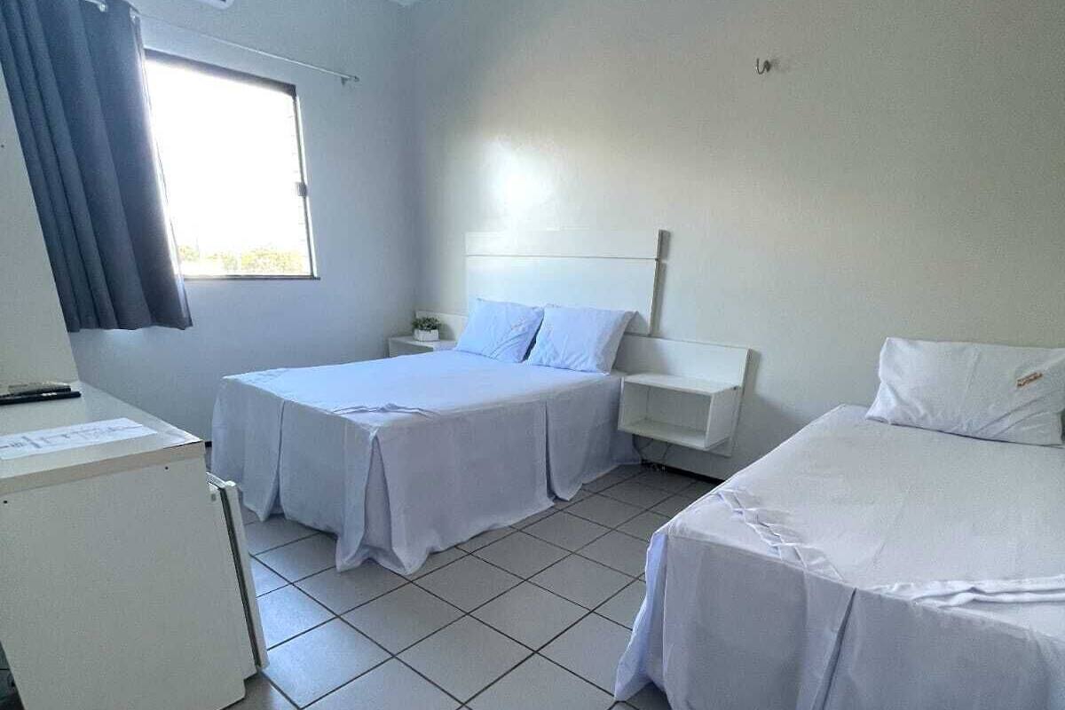 A hotel room with two single beds, a small desk, and a refrigerator.